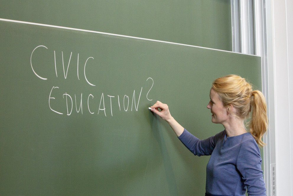 Inken Heldt schreibt mit Kreide Civic Education auf eine Tafel 