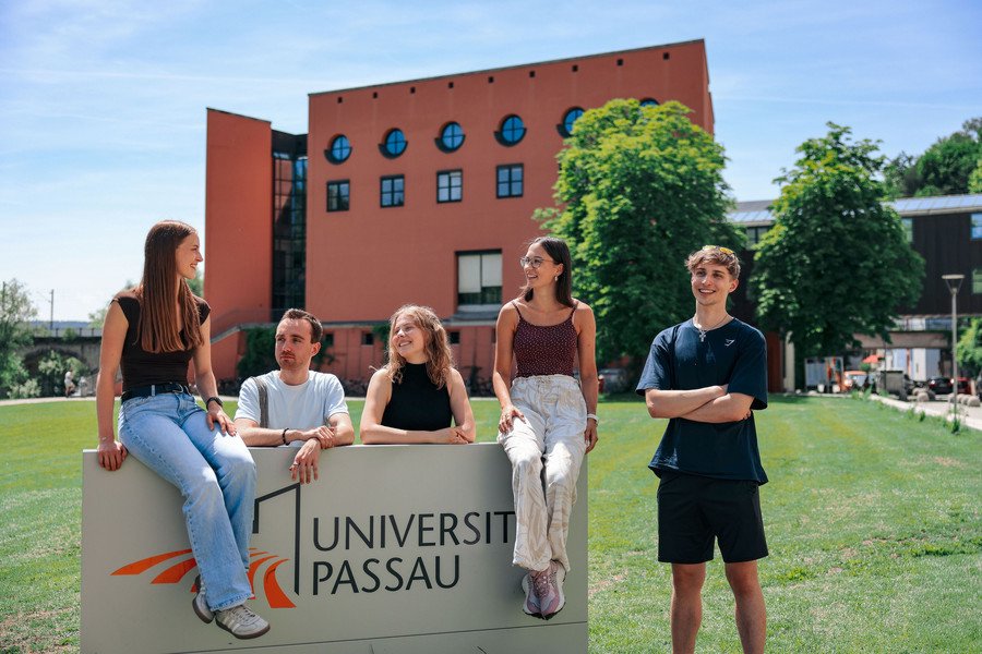 Studierende vor dem Campuslogo der Universität Passau; Foto: Universität Passau.