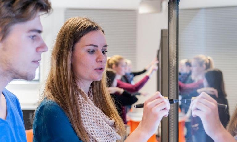 Studierende im Bereich Kommunikation schreiben auf Smartboard